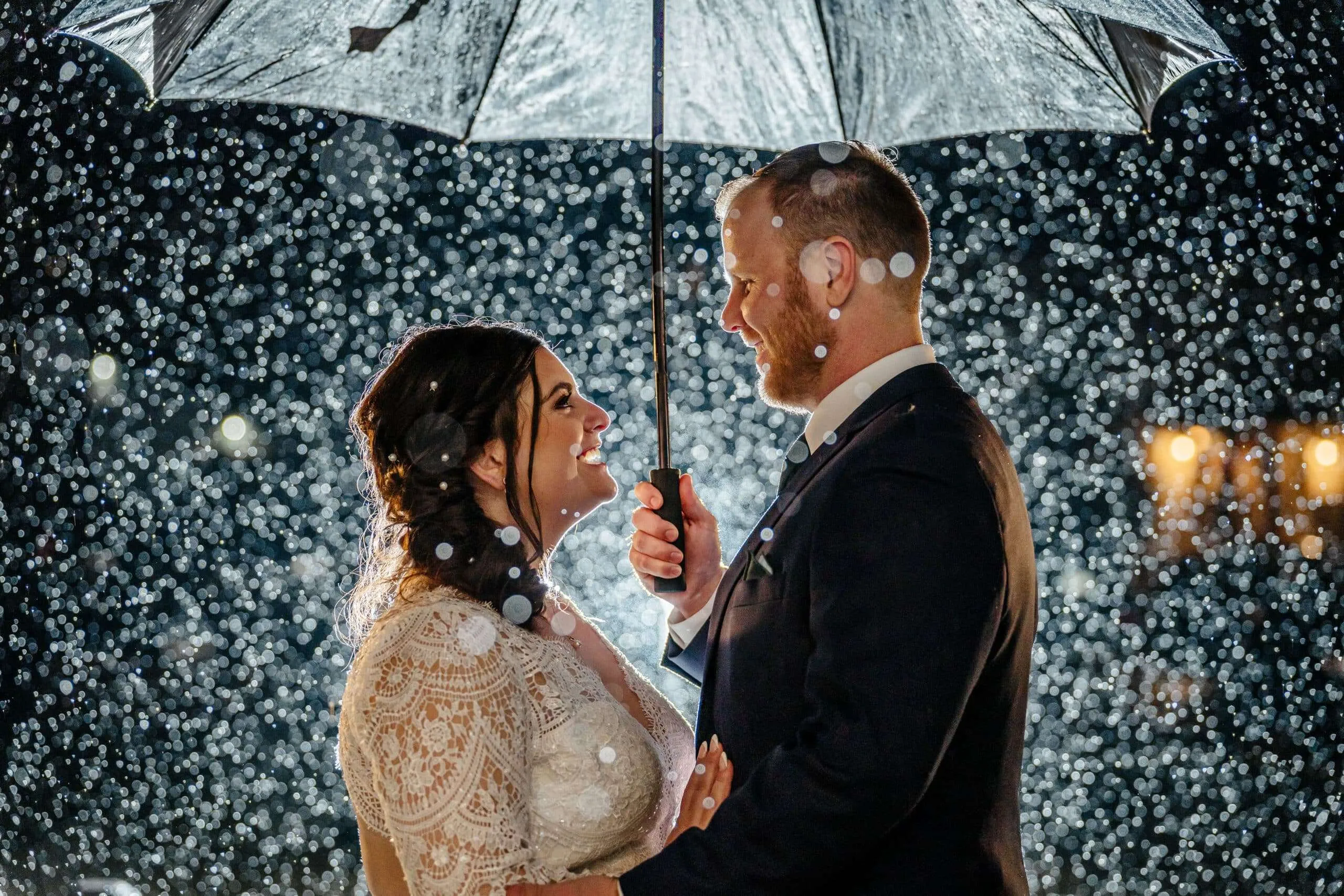 A romantic wedding couple sharing a moment under an umbrella in the rain, photographed by a wedding photographer in New England.