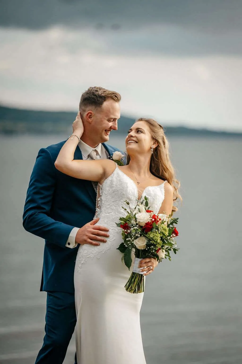 A bride and groom embracing on a scenic shoreline, captured by a professional wedding photographer in New England.